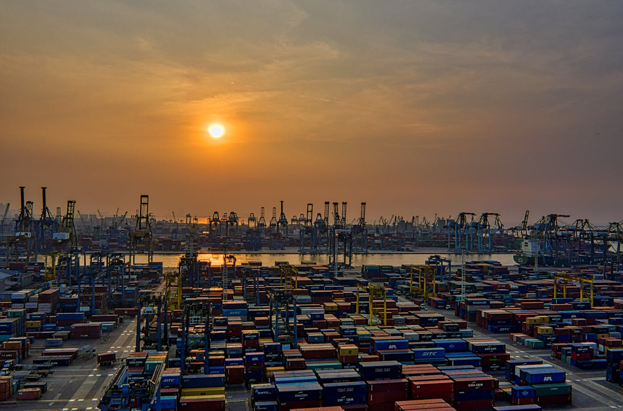 service-02 Sunset over a bustling seaport filled with stacked shipping containers and cranes.
